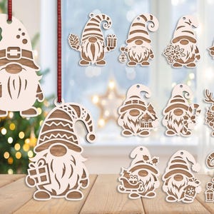 Puede incluir: Una colección de doce adornos de gnomos de madera cortados con láser que presentan varios diseños con temática navideña, incluidos regalos, bastones de caramelo, árboles y linternas. Cada adorno tiene un acabado de madera clara con vetas oscuras.