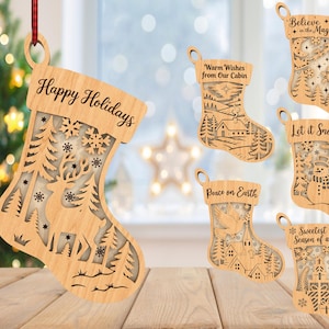 May include: Wooden Christmas stocking ornaments with intricate cut-out designs. One ornament reads "Happy Holidays" and features a deer and trees. Other ornaments have holiday-themed text like "Believe in the Magic" and "Let it Snow".