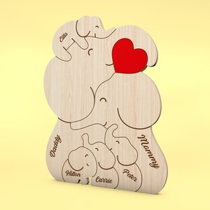 Op de afbeelding: Houten olifantenfamilie-uitsparing met een rood hart. De namen "Daddy", "Mommy", "Ellis", "Hilton", "Carrie" en "Peter" zijn gegraveerd. De olifantenfamilie is gemaakt van lichtgekleurd hout.