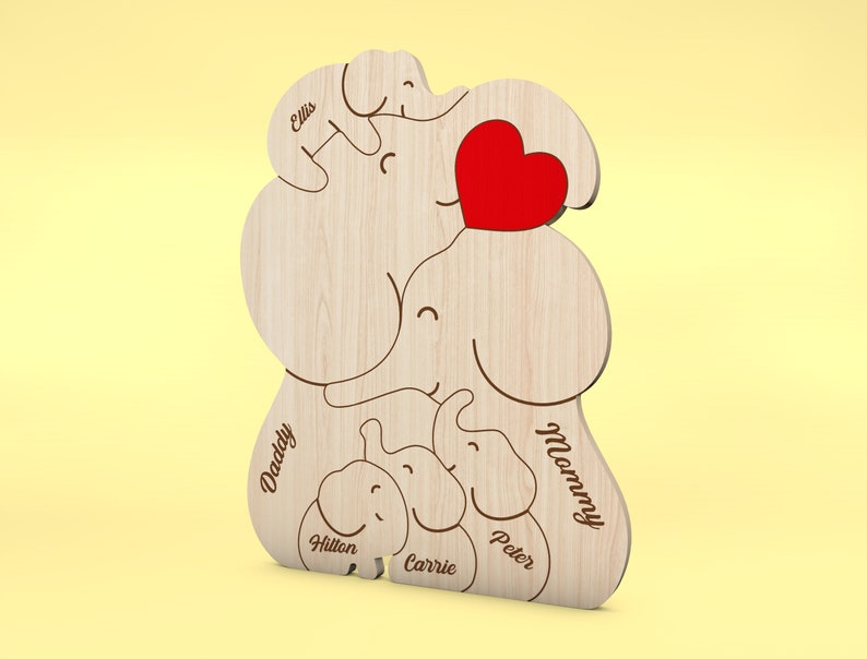 Op de afbeelding: Houten olifantenfamilie-uitsparing met een rood hart. De namen "Daddy", "Mommy", "Ellis", "Hilton", "Carrie" en "Peter" zijn gegraveerd. De olifantenfamilie is gemaakt van lichtgekleurd hout.