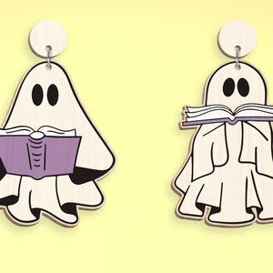 Op de afbeelding: Twee witte spookornamenten met zwarte ogen en monden. Een spook houdt een paars boek vast en het andere houdt een wit boek vast met de tekst "Read" erop.