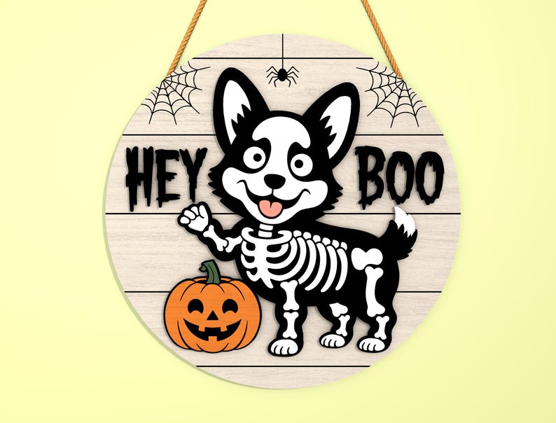 Może przedstawiać: Okrągły drewniany znak na Halloween z kresk&oacute;wkowym szkieletem corgi i dynią. Znak głosi "HEY BOO" czarnymi literami, z pajęczynami i pająkiem na g&oacute;rze. Znak jest zawieszony na brązowej linie.