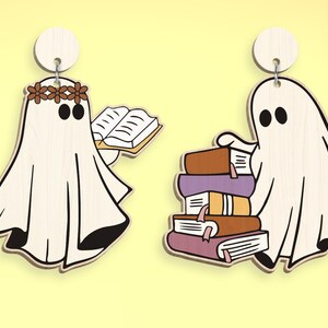 Op de afbeelding: Twee witte spookornamenten met zwarte ogen. E&eacute;n spook houdt een boek vast en draagt een bruine bloemenkrans. Het andere spook houdt een stapel kleurrijke boeken vast.