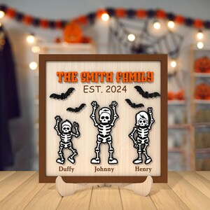 May include: A brown wooden sign with the text "The Smith Family Est. 2024" and three black skeleton figures with the names "Duffy", "Johnny", and "Henry" underneath.