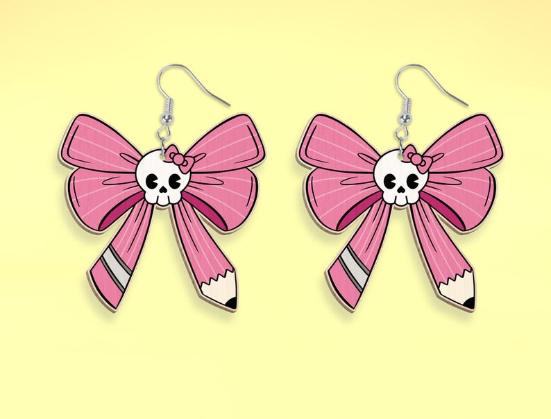 May include: A pair of pink bow earrings with a skull charm and a small pink bow on the skull. The bow has a pencil-shaped detail on the bottom.