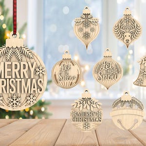 May include: A selection of wooden Christmas decorations in diverse shapes, such as bells and teardrops. The ornaments display detailed cut-out patterns, snowflakes, and the phrases "Merry Christmas" and "Let it Snow".