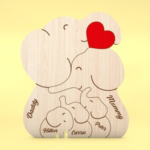 Op de afbeelding: Houten familie-olifantvormige decoratie met een rood hart. Het ontwerp bevat de woorden "Daddy" en "Mommy", samen met de namen "Hilton", "Carrie" en "Peter". De olifantenfamilie is gemaakt van lichtgekleurd hout.