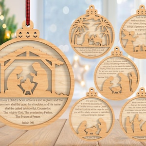 May include: Wooden Christmas ornaments with Nativity scenes. Each ornament is round with a cutout design and a scripture quote. The ornaments are made of light-colored wood and have a small hole at the top for hanging. A red and black plaid ribbon is attached to one.