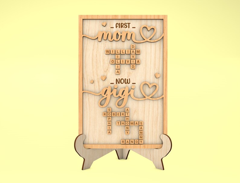 May include: Wooden sign with the words "FIRST - mom" and "NOW - gigi" in a cursive font. The words are surrounded by hearts. The sign also features a crossword puzzle with the names "William", "Olivia", "Robert", "Sophia", "Thomas", "Randy", and "Sammy".