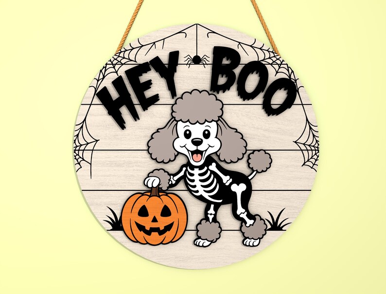 Może przedstawiać: Okrągły drewniany znak na Halloween z napisem "HEY BOO". Kresk&oacute;wkowy pudel w kostiumie szkieletu trzyma pomarańczową dynię. Znak ma wz&oacute;r pajęczyny i jest zawieszony na brązowej linie.