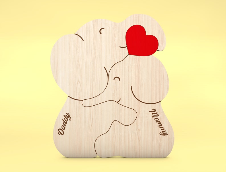 Op de afbeelding: Houten puzzel in de vorm van een olifant met een rood hart en de woorden "Daddy" en "Mommy". De puzzel is gemaakt van lichtgekleurd hout met een gladde afwerking. Het ontwerp toont twee olifanten die elkaar omarmen, met een hart ertussen.