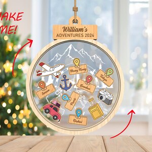 Può includere: Un ornamento natalizio in legno con un globo di plastica trasparente che può essere agitato per rivelare diverse destinazioni di viaggio. L'ornamento è personalizzato con il nome "William's Adventures 2024".
