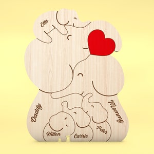 Op de afbeelding: Houten decoratie met een olifantenfamilie thema en een rood hart. De namen "Daddy", "Mommy", "Ellis", "Hilton", "Carrie" en "Peter" zijn gegraveerd op het houten oppervlak. Het ontwerp toont een olifantenfamilie.