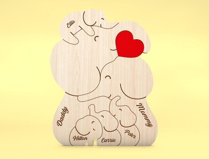 Op de afbeelding: Houten decoratie met een olifantenfamilie thema en een rood hart. De namen "Daddy", "Mommy", "Ellis", "Hilton", "Carrie" en "Peter" zijn gegraveerd op het houten oppervlak. Het ontwerp toont een olifantenfamilie.