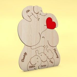 Op de afbeelding: Houten decoratie met olifantenfamilie thema, gegraveerde namen en een rood hart. De namen "Daddy", "Mommy", "Peter", "Carrie", "Hilton" en "Ellis" zijn gegraveerd op de olifantenfiguren. De decoratie is gemaakt van lichtgekleurd hout.