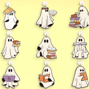 Op de afbeelding: Negen witte spookornamenten met verschillende boekthema's. Sommige spoken houden boeken vast, andere hebben boeken op hun hoofd en weer andere hebben stapels boeken. De spoken zijn allemaal wit met zwarte ogen en een zwarte mond.