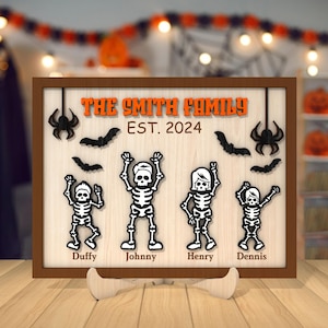 May include: A wooden sign with a black and white Halloween theme. The sign says "The Smith Family Est. 2024" and features four skeletons with names: Duffy, Johnny, Henry, and Dennis.