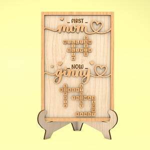 May include: Wooden sign with the words "FIRST - mom" and "NOW - ginny" in a heart-shaped frame. The sign features a scrabble tile crossword puzzle with names like William, Olivia, Robert, Sophia, Thomas, and Randy.