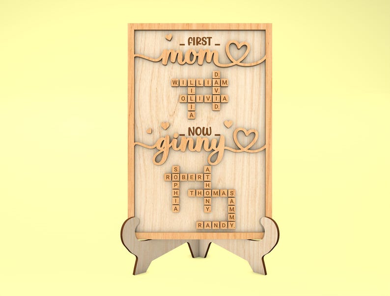 May include: Wooden sign with the words "FIRST - mom" and "NOW - ginny" in a heart-shaped frame. The sign features a scrabble tile crossword puzzle with names like William, Olivia, Robert, Sophia, Thomas, and Randy.