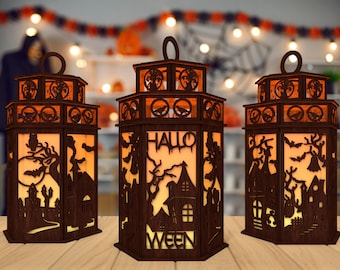 Peut inclure: Trois lanternes d'Halloween en bois avec des découpes complexes de chauves-souris, d'arbres et d'une maison hantée. Les lanternes sont éclairées de l'intérieur, projetant une lueur chaude. La lanterne du milieu porte le texte "Hallo Ween".