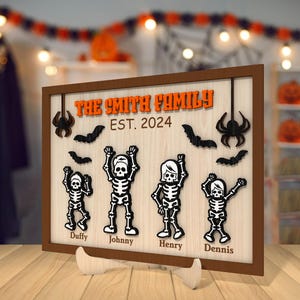 May include: A wooden sign with a Halloween theme featuring a family of skeletons. The sign reads "The Smith Family Est. 2024" and features the names "Duffy, Johnny, Henry, and Dennis".
