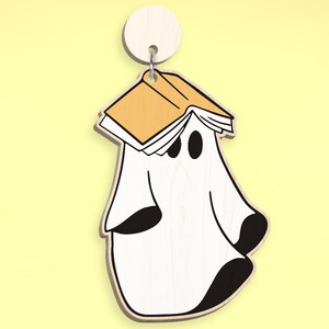 Op de afbeelding: Een witte geest met zwarte ogen draagt een geel boek op zijn hoofd. De geest is een houten ornament.