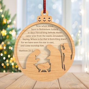 May include: Wooden Christmas ornament with a nativity scene cutout and the text "Now when Jesus born in Bethlehem Judaea...Matthew 2:1-2". The ornament is round with a decorative top and a red and black plaid ribbon for hanging.