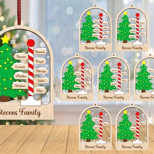 Puede incluir: Un conjunto de ocho adornos navideños de madera con un diseño de bola de nieve con un árbol de Navidad verde y un bastón de caramelo rojo y blanco. Cada adorno tiene un nombre personalizado en un letrero y el texto "Stevens Family".