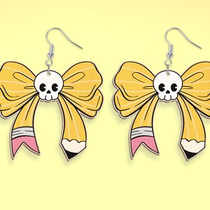 May include: A pair of yellow bow earrings with a skull in the center of the bow. The bow is shaped like a pencil with a pink eraser and a black pencil tip.