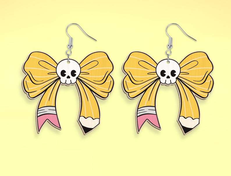 May include: A pair of yellow bow earrings with a skull in the center of the bow. The bow is shaped like a pencil with a pink eraser and a black pencil tip.