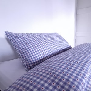 May include: A blue and white checked bedspread with a red heart pattern. The bedspread is on a bed with a white pillow.