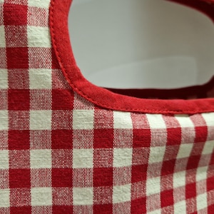 close up photo of a beautiful gingham red checked fabric for a cotton clothes page bag. In closer detail the peg back has a plain red fabric piping around the peg bag opening.