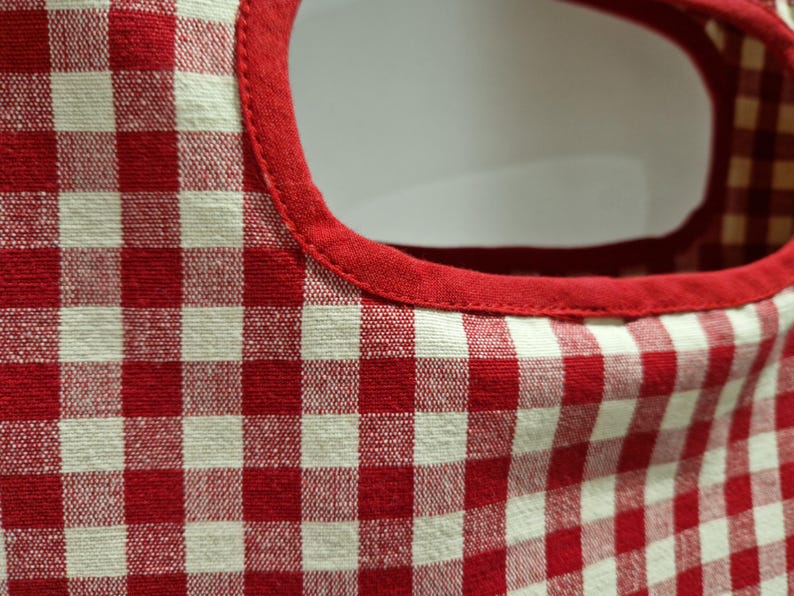 close up photo of a beautiful gingham red checked fabric for a cotton clothes page bag. In closer detail the peg back has a plain red fabric piping around the peg bag opening.