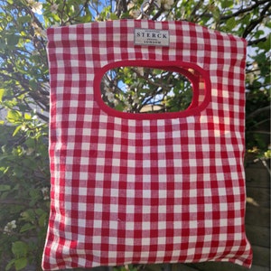 Cotton peg bag in a red gingham check fabric hanging from a garden tree.
