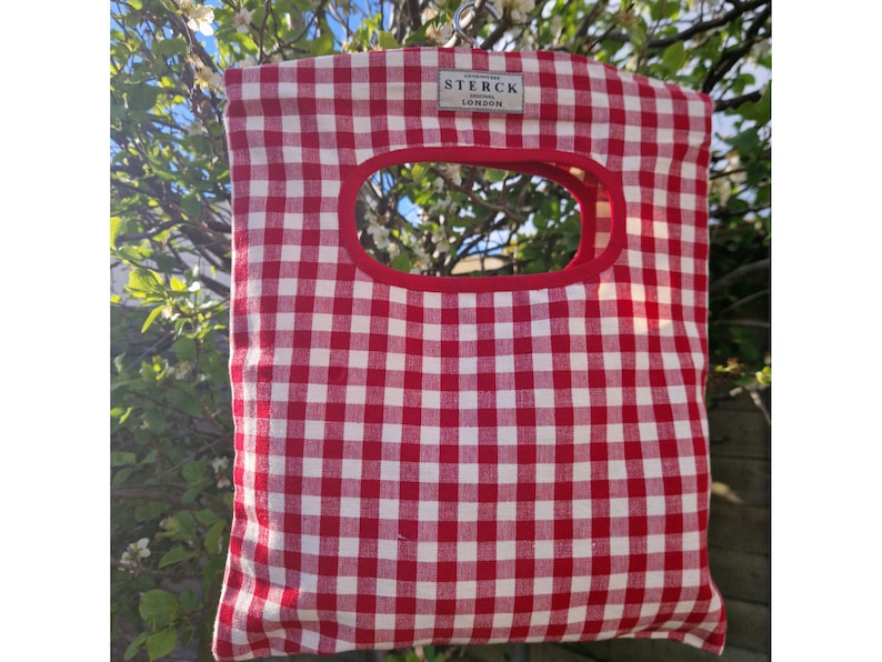 Cotton peg bag in a red gingham check fabric hanging from a garden tree.