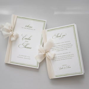 Könnte beinhalten: Zwei weiße Hochzeitsprogramme mit salbeigrünen Rändern und cremefarbenen Seidenbandschleifen. Die linke Karte zeigt den Text Welcome to the wedding of Emilia and Thomas, 18 January 2025, London, England. Die rechte Karte zeigt den Text Thank you.