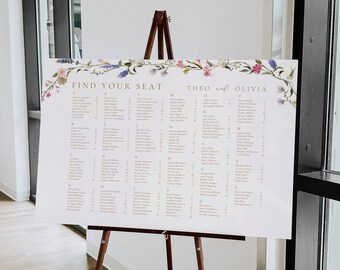 May include: A white wedding seating chart with a floral border. The chart is on an easel and lists the names of guests in alphabetical order. The text at the top reads "Find Your Seat" and "Theo and Olivia".