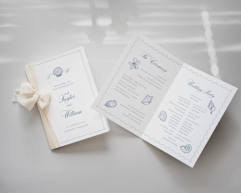 May include: A folded wedding program and a matching card featuring blue seashell illustrations, navy blue text, and a cream-colored ribbon. The text includes "Welcome to the Wedding of Taylor and William," "The Ceremony," and "Wedding Party."
