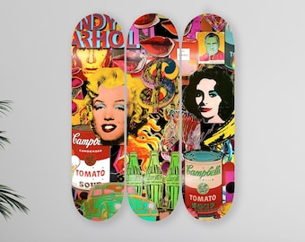 Op de afbeelding: Drie skateboard decks met een collage van afbeeldingen, waaronder Andy Warhols iconische Campbell's soepblikken, Marilyn Monroe en een Coca-Cola fles. De decks zijn verticaal gerangschikt en hebben een levendig kleurenpalet.