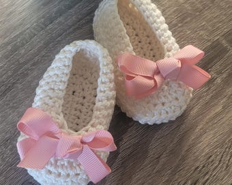 May include: A pair of white crocheted baby shoes with pink bows. The shoes are made with a delicate crochet stitch and have a soft, comfortable feel.