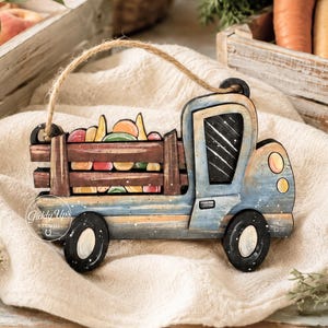May include: A blue wooden truck cutout with a brown cargo bed filled with colorful produce, featuring a jute twine hanger and black wheels. The text SVG DIGITAL DOWNLOAD. NO PHYSICAL ITEM WILL BE SENT. is printed on the right side of the image.