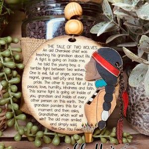 May include: Wooden ornament with a Native American design and a quote about the tale of two wolves. The quote reads "The Tale of Two Wolves. An old Cherokee chief was teaching his grandson about life. A fight is going on inside me, he told the young boy, a terrible fight between two wolves. One is evil, full of anger, sorrow, regret, greed, self-pity and false pride. The other is good, full of joy, peace, love, humility, kindness and faith. This same fight is going on inside of you, grandson and inside of every other person on this earth. The grandson ponders this for a moment and then asks, Grandfather, which wolf will win? The old man smiled and simply said, The One You Feed."