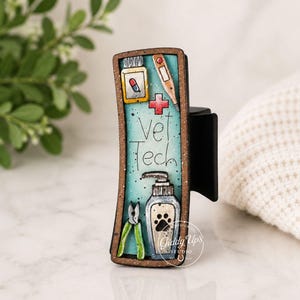May include: A black hair clip with a rectangular design featuring veterinary-themed illustrations. The design includes a pill, thermometer, cross, and the words "Vet Tech." Additional images include a bottle of soap and a paw print.