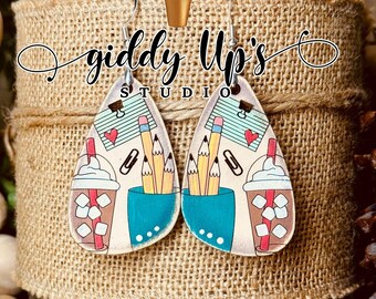 May include: A pair of dangle earrings with a light brown background. One earring features a cup of coffee with marshmallows and a pencil holder with pencils. The other earring features a notepad with a paperclip, a heart, and pencils. The earrings are labeled "giddy Up's Studio".