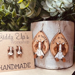 Puede incluir: Un par de pendientes de madera con un diseño de cabra. Los pendientes tienen forma de lágrima y llevan la inscripción "Not a Sheep". Los pendientes están hechos a mano y vienen con un par de pendientes de cabra más pequeños.