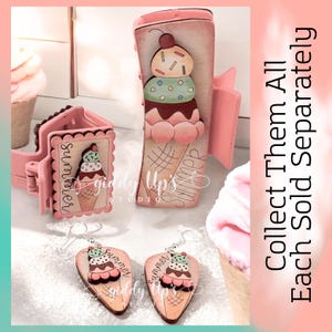 May include: A set of three wooden ice cream cone themed crafts. The set includes a hair clip, a small sign, and a pair of earrings. The hair clip and sign are painted pink and feature a three-scoop ice cream cone with sprinkles. The earrings are painted in a similar style and feature the text "Summer".