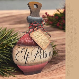 May include: Wooden Elf Potion bottle with a red and brown color scheme. The bottle has a wooden handle and a tag that reads "Warning May cause Pointy Ears." The bottle is decorated with a green and red twine bow. The words "Elf Potion" are written on the bottle.