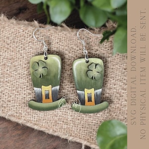 May include: A pair of green wooden earrings shaped like leprechaun hats, each with a silver hook and a carved shamrock. The hats have gold and silver accents. The earrings are displayed on a burlap surface.