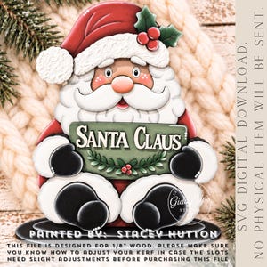 May include: A decorative Santa Claus cutout featuring a red hat with white trim, a white beard, and black gloves. Santa holds a green sign with the text SANTA CLAUS and holly accents. The text SVG DIGITAL DOWNLOAD NO PHYSICAL ITEM WILL BE SENT is visible.