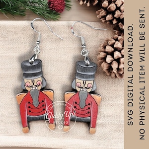 Puede incluir: Pendientes de madera con diseño de cascanueces. Los pendientes tienen una chaqueta roja, sombrero negro y ganchos plateados. El texto "SVG DIGITAL DOWNLOAD. NO PHYSICAL ITEM WILL BE SENT." es visible.